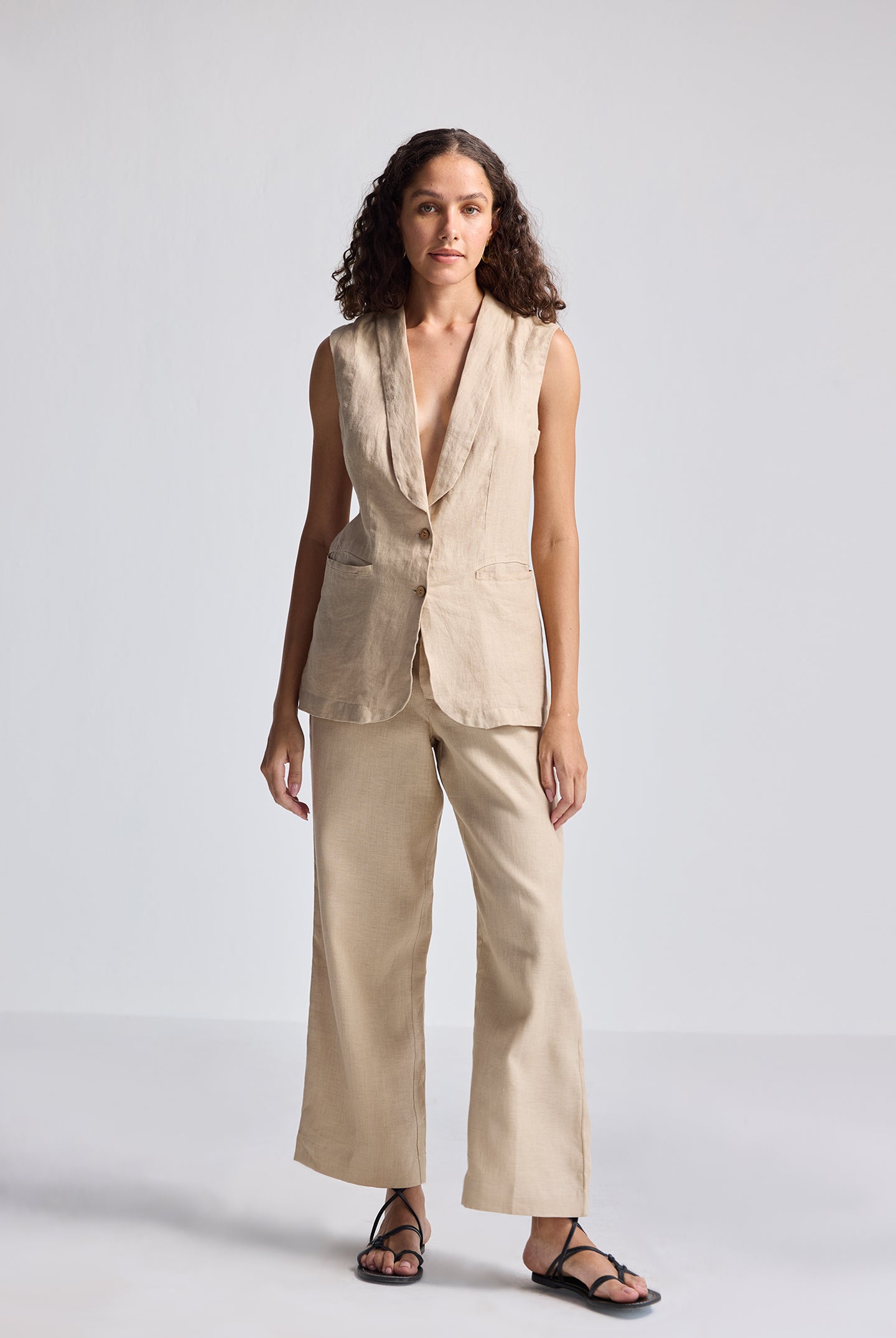 Full-length studio shot of model wearing Reistor Sleeveless Hemp Jacket Set in natural beige, featuring a sleeveless tailored hemp jacket with button detailing paired with wide-leg hemp trousers for sustainable women’s fashion.