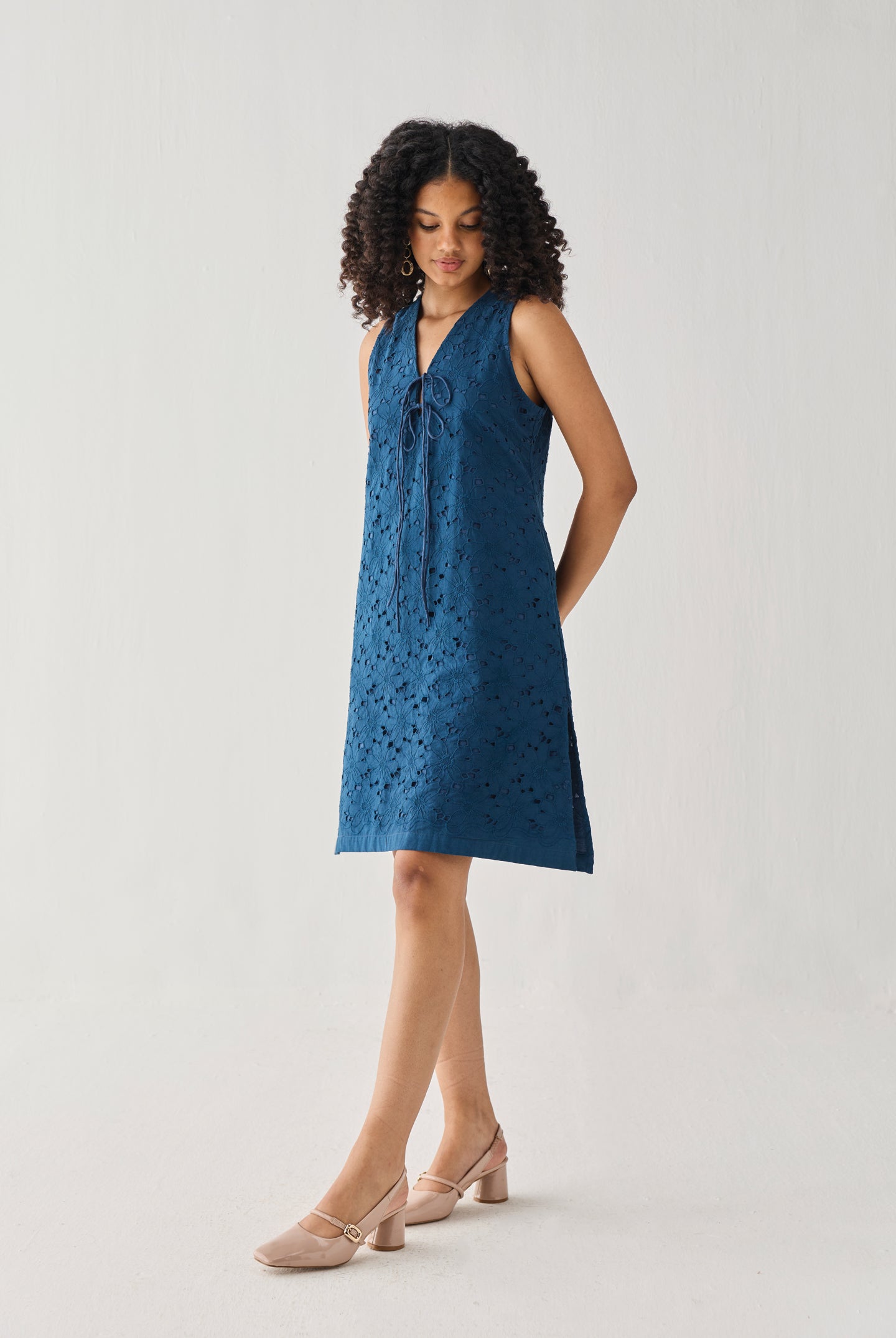 Sleeveless Knee-Length Dress in Blue with eyelet embroidery, a V-neck tie detail, and an easy A-line silhouette, shown in a full-length studio portrait.