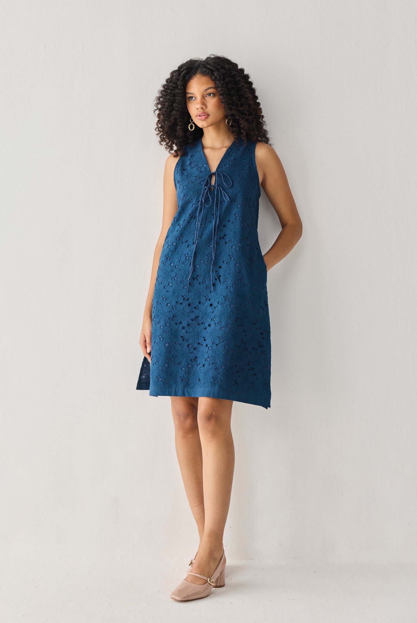Sleeveless Knee-Length Dress in Blue with eyelet embroidery, V-neck tie detail, and a relaxed silhouette, shown in a full-length studio portrait.