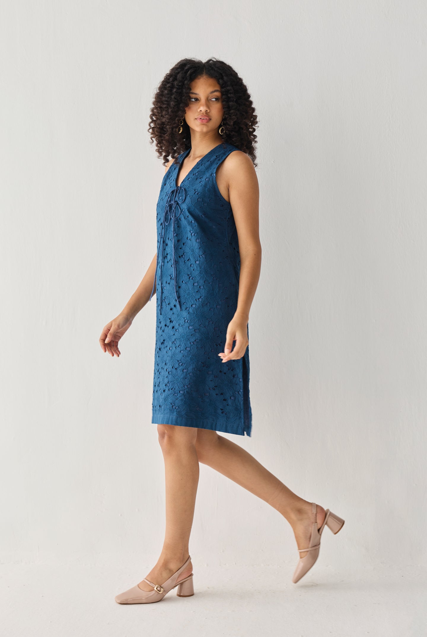 Sleeveless Knee-Length Dress in Blue with eyelet embroidery, a V-neck tie detail, and a relaxed silhouette, shown in motion in a full-length studio view.