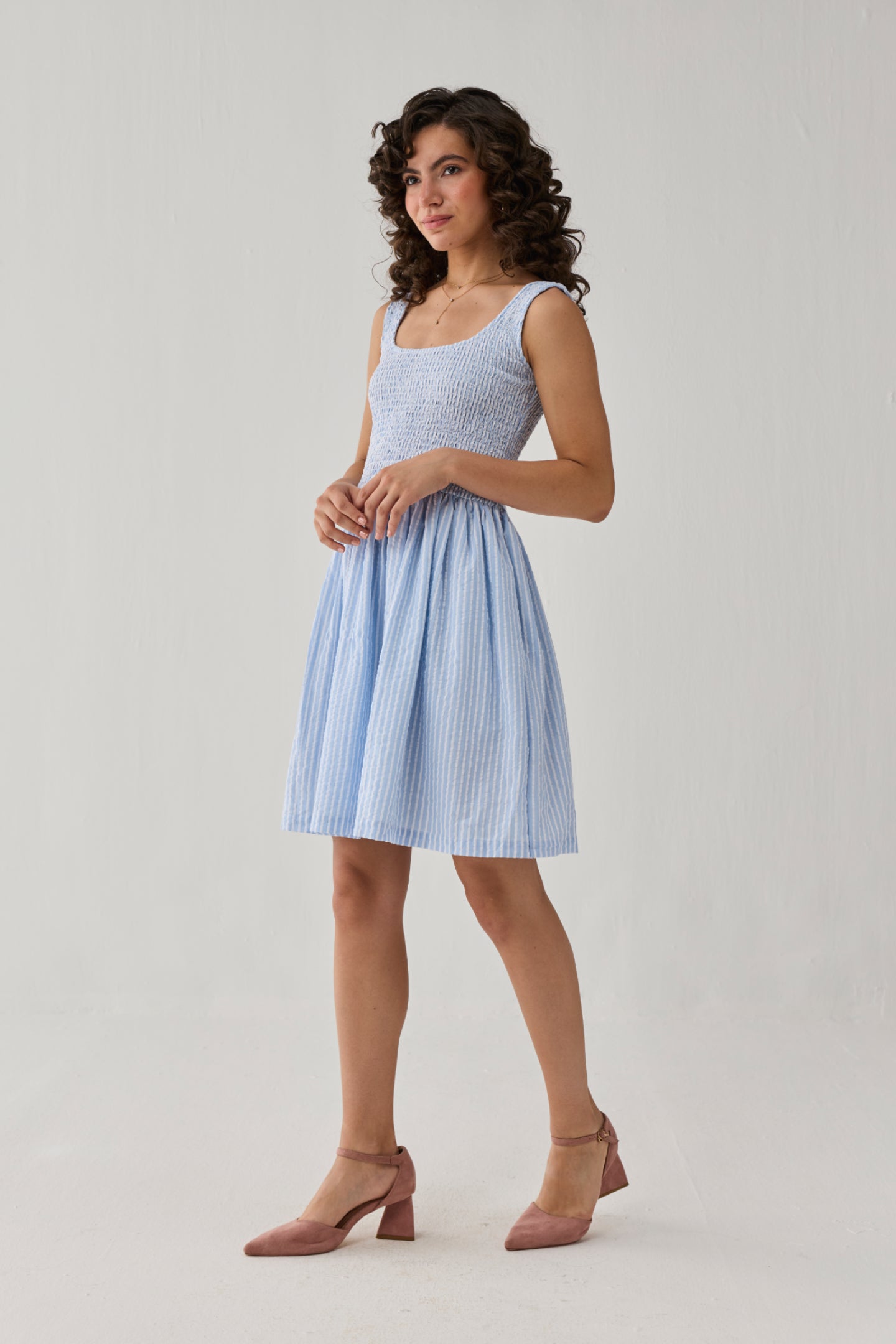 Smocked Short Dress in Blue Stripes offering timeless charm with a gathered waistline, airy striped fabric, and graceful feminine appeal.