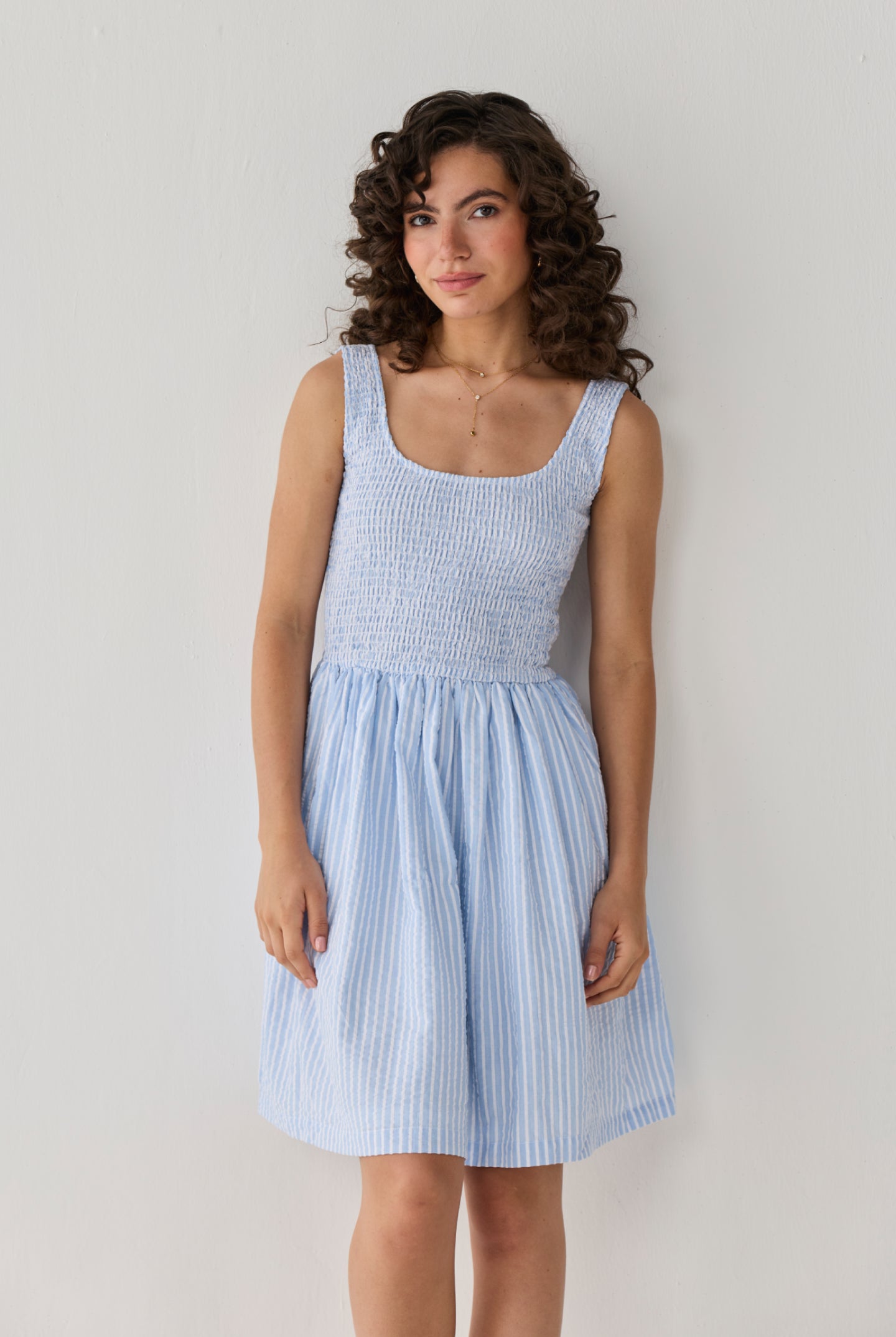 Smocked Short Dress in Blue Stripes designed with a fitted textured bodice and airy striped skirt, creating a timeless casual-chic outfit.