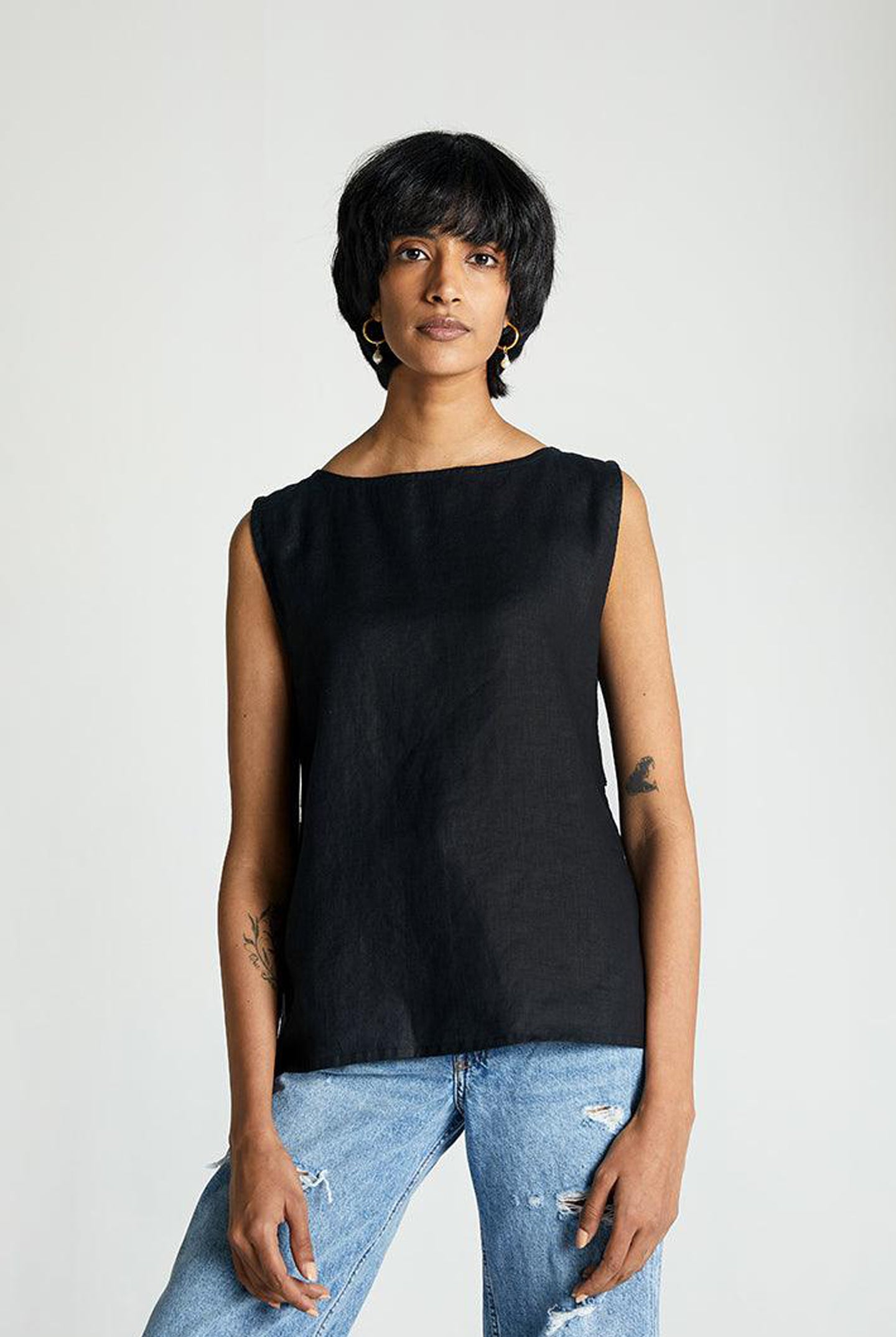 A woman wearing a sleeveless black top with eyelet buttons at the back, paired with blue jeans.