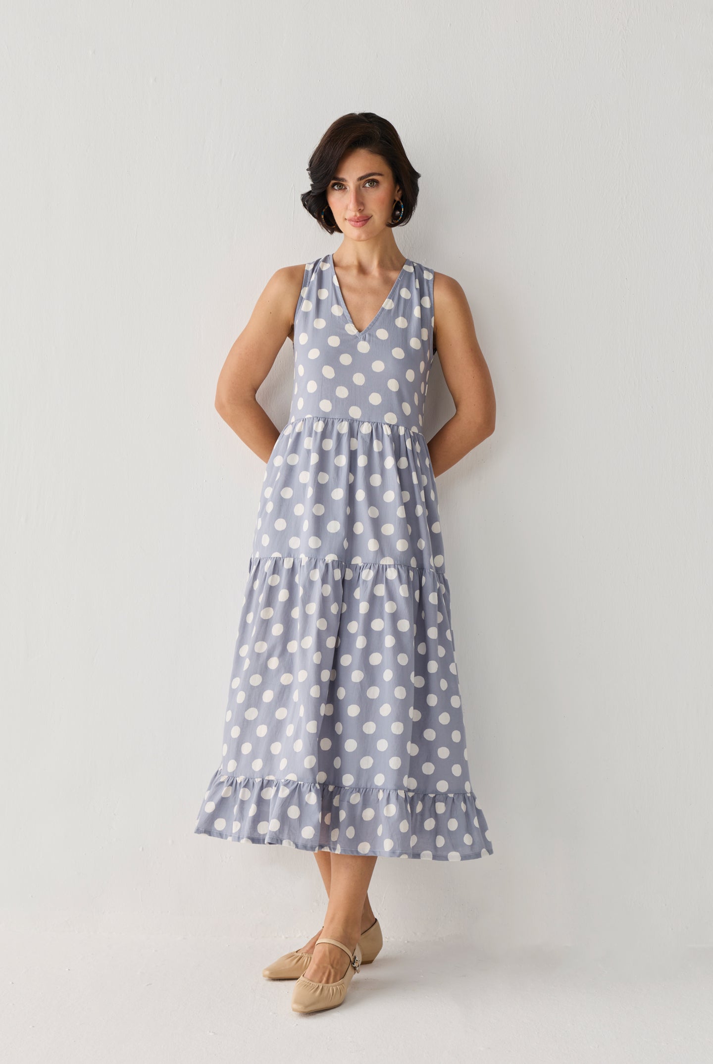 Tiered Midi Dress in Blue Polka featuring a sleeveless design, V-neckline, and flowing tiered skirt with white polka dots, shown in a full-length studio portrait.