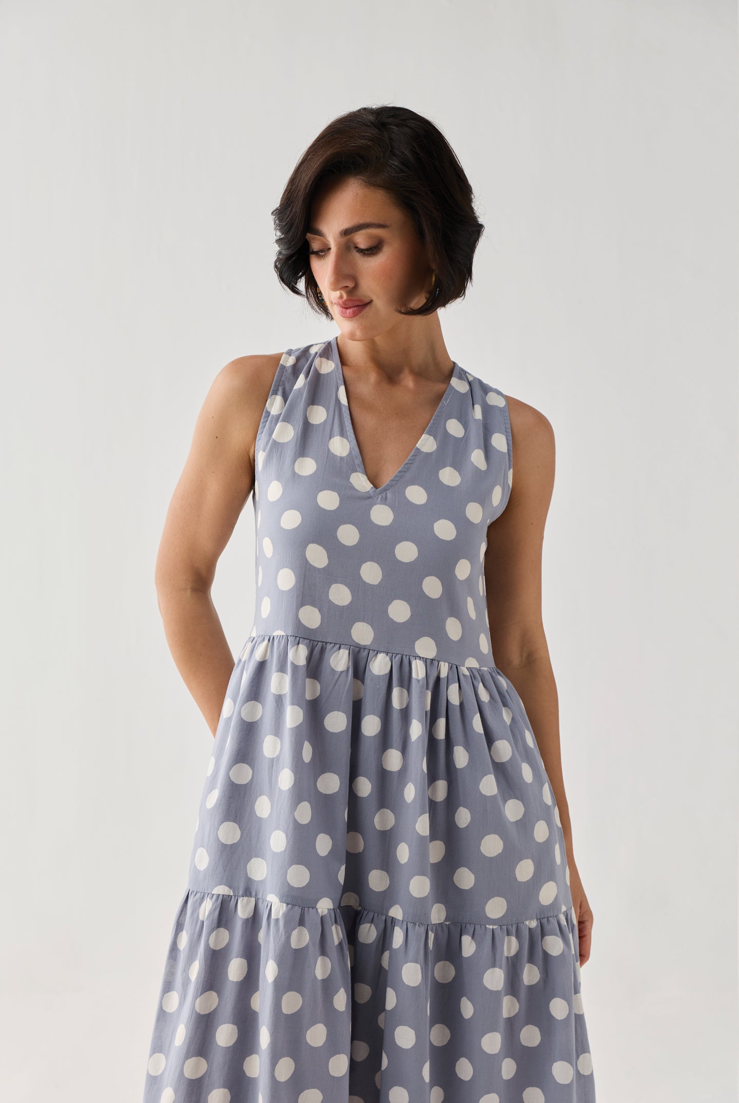 Tiered Midi Dress in Blue Polka featuring a sleeveless V-neck design, white polka dot print, and flowing tiered skirt, shown in a close-up studio view.
