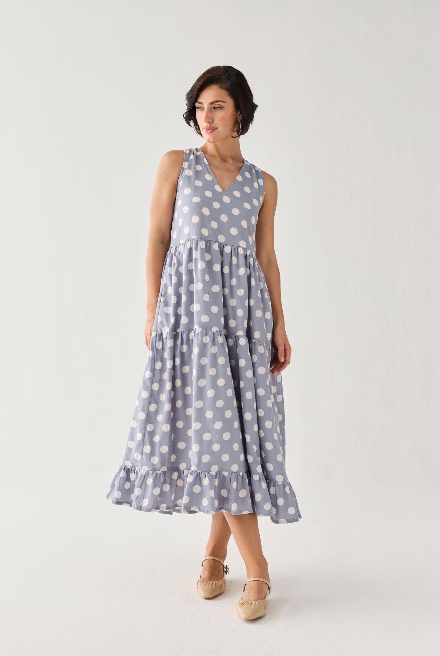 Tiered Midi Dress in Blue Polka with oversized white dots, a sleeveless V-neck bodice, and a swaying layered skirt, captured mid-step to showcase its fluid movement.