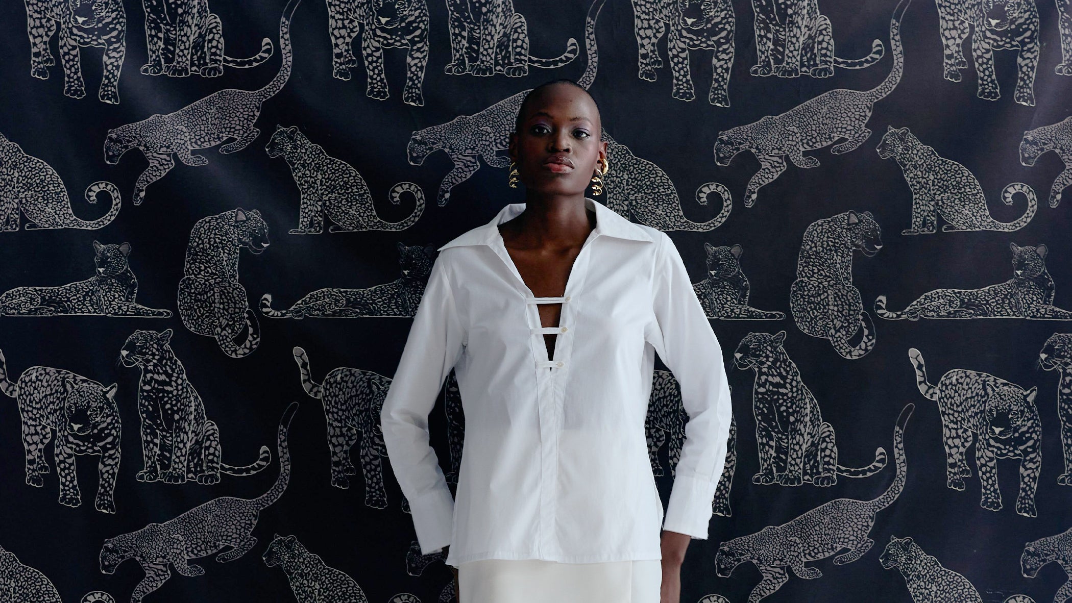 Woman in a white shirt standing against a patterned wall with animal silhouettes.