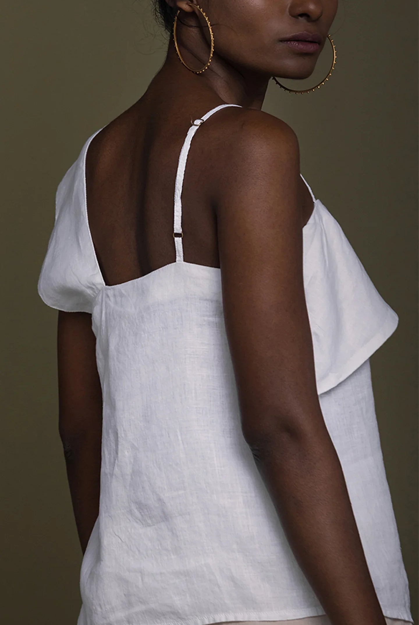 Woman wearing a Reistor white top with thin straps against a brown background.