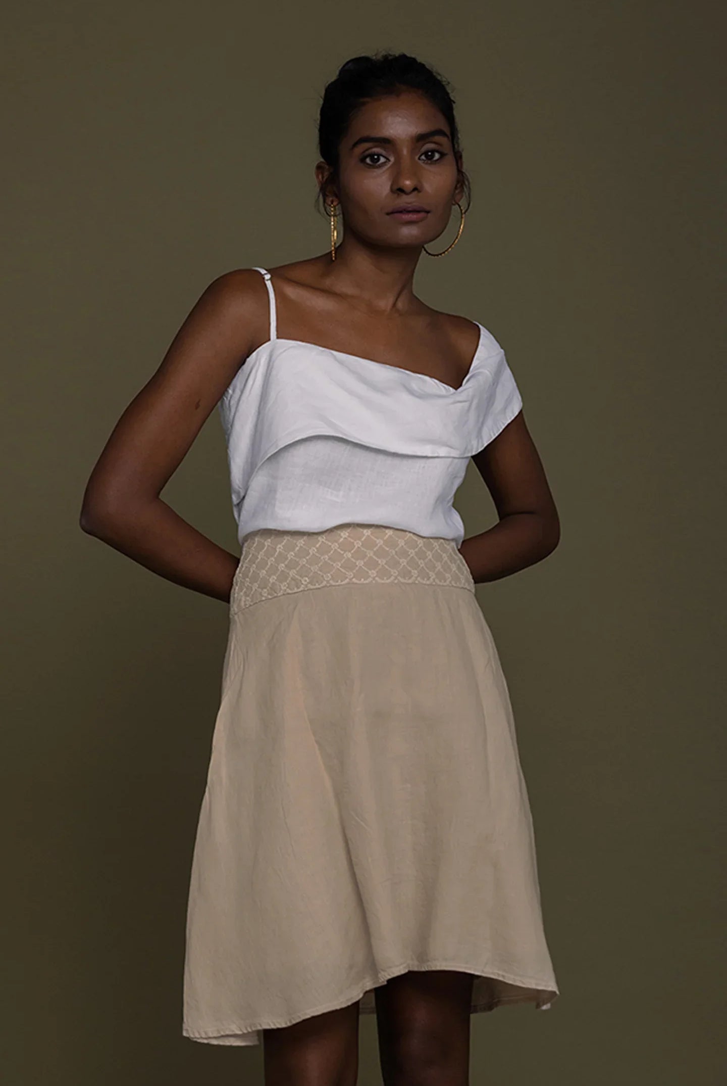 Woman wearing a Reistor white top and beige skirt against a brown background.