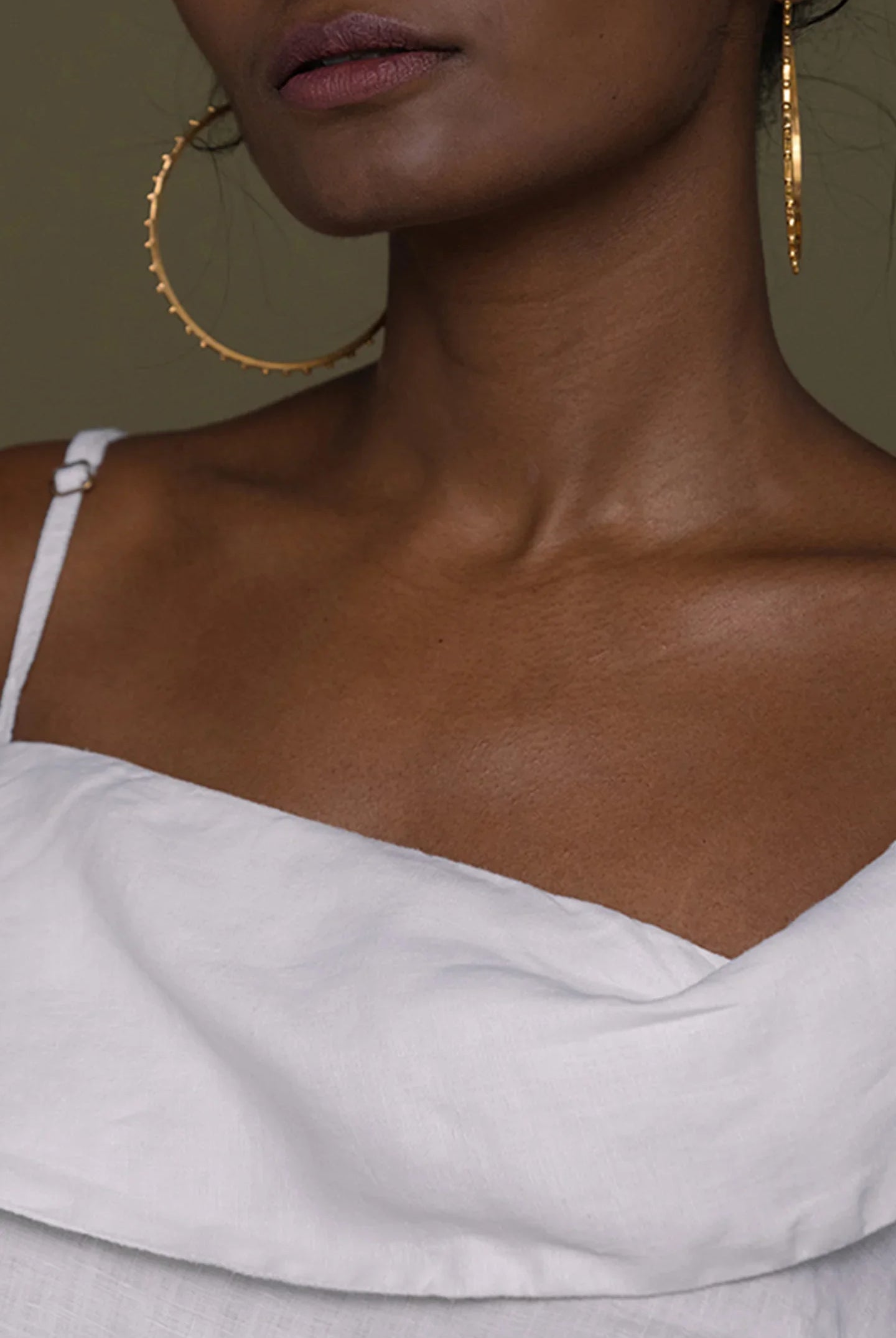 Close-up of a person wearing Reistor gold hoop earrings and a white top.