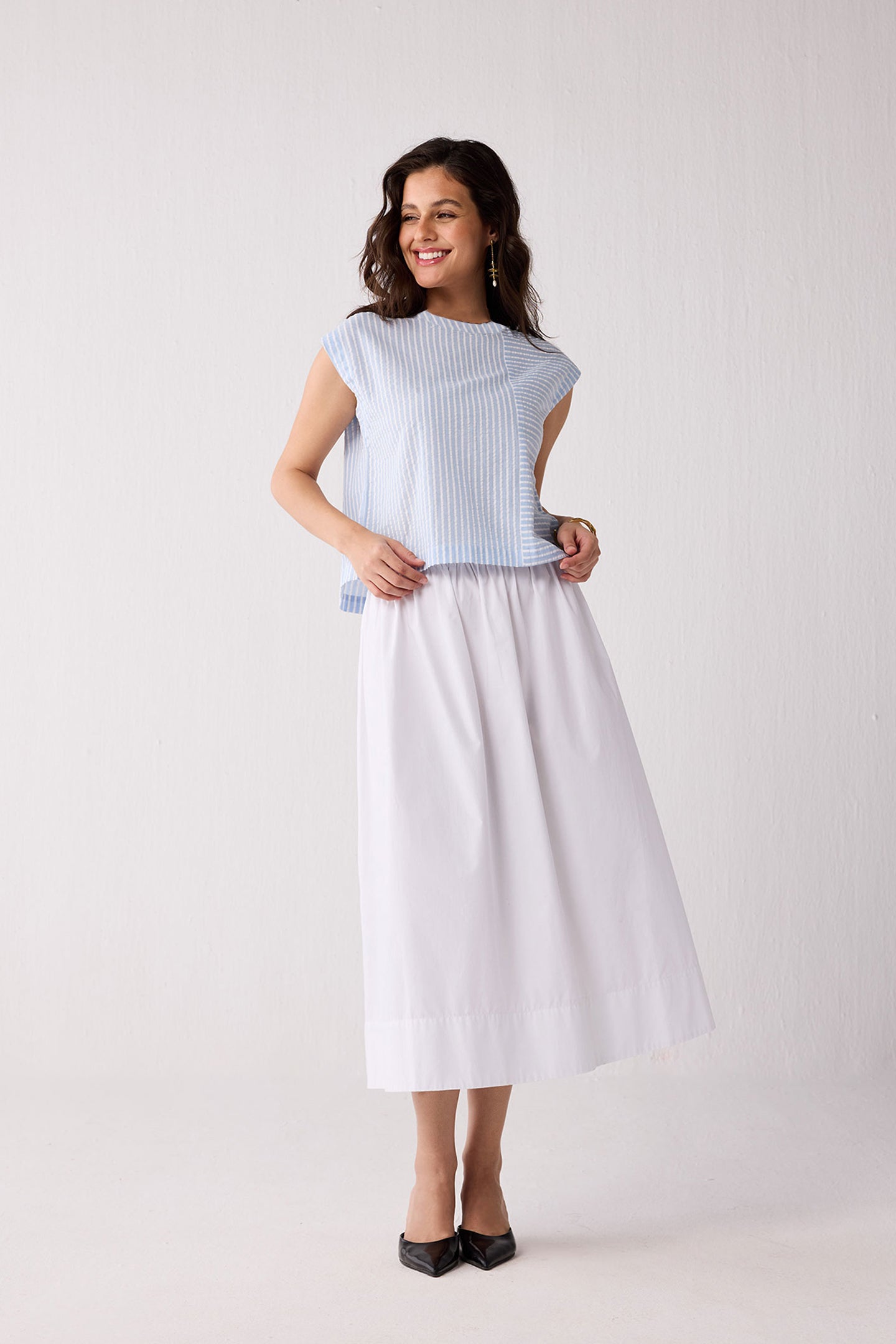 A woman wearing a light blue striped top and a white skirt on a plain background