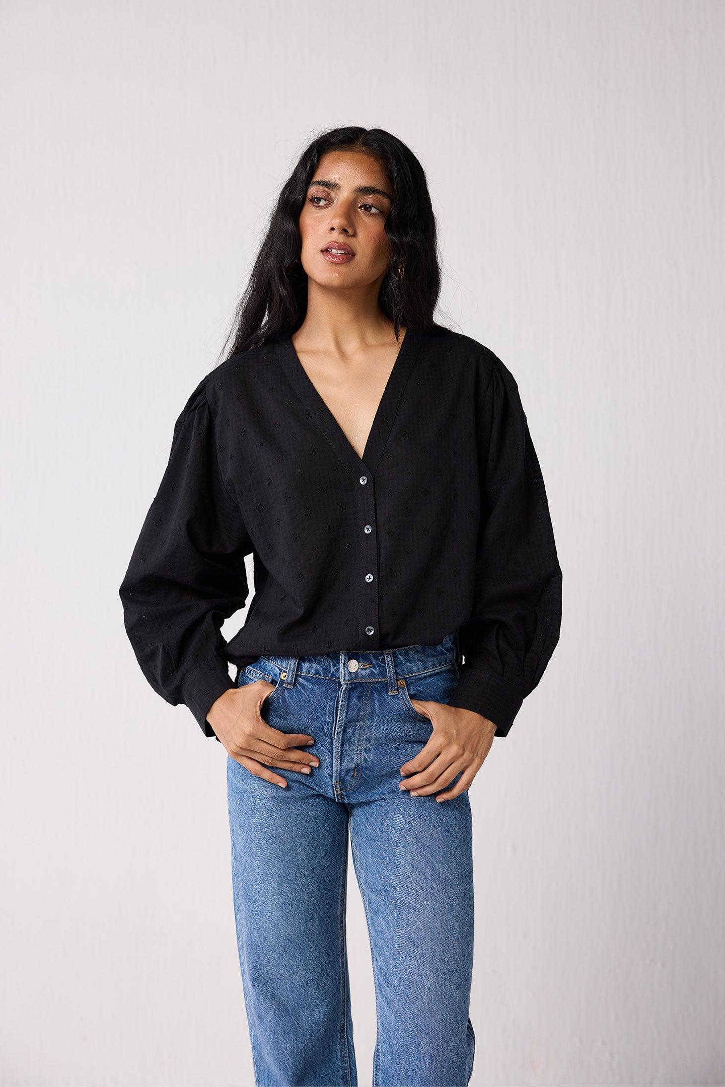 Woman wearing a black blouse and blue jeans against a white background