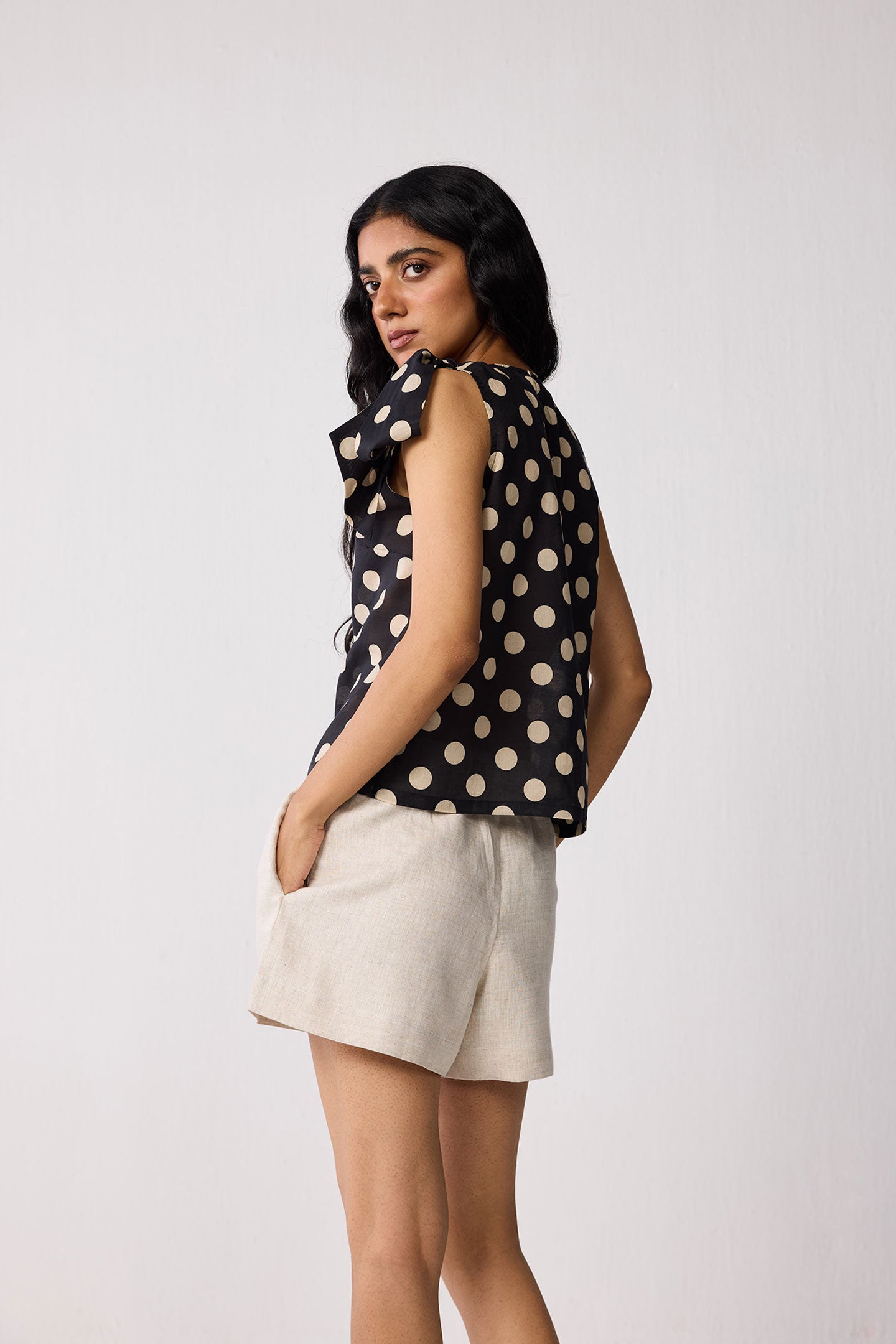 Woman wearing a black sleeveless top with beige polka dots and beige shorts on a white background