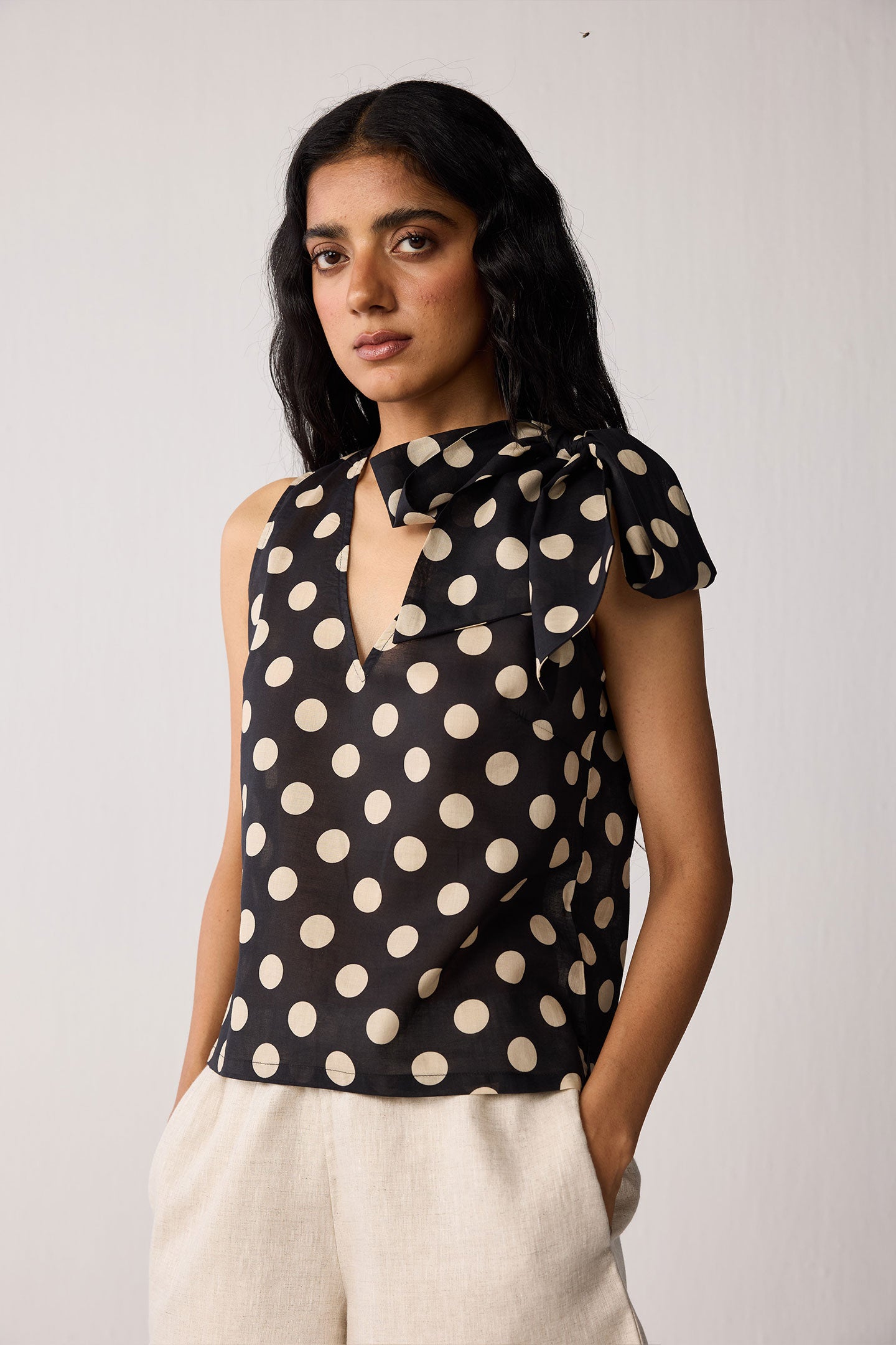 Woman wearing a black sleeveless top with beige polka dots on a white background