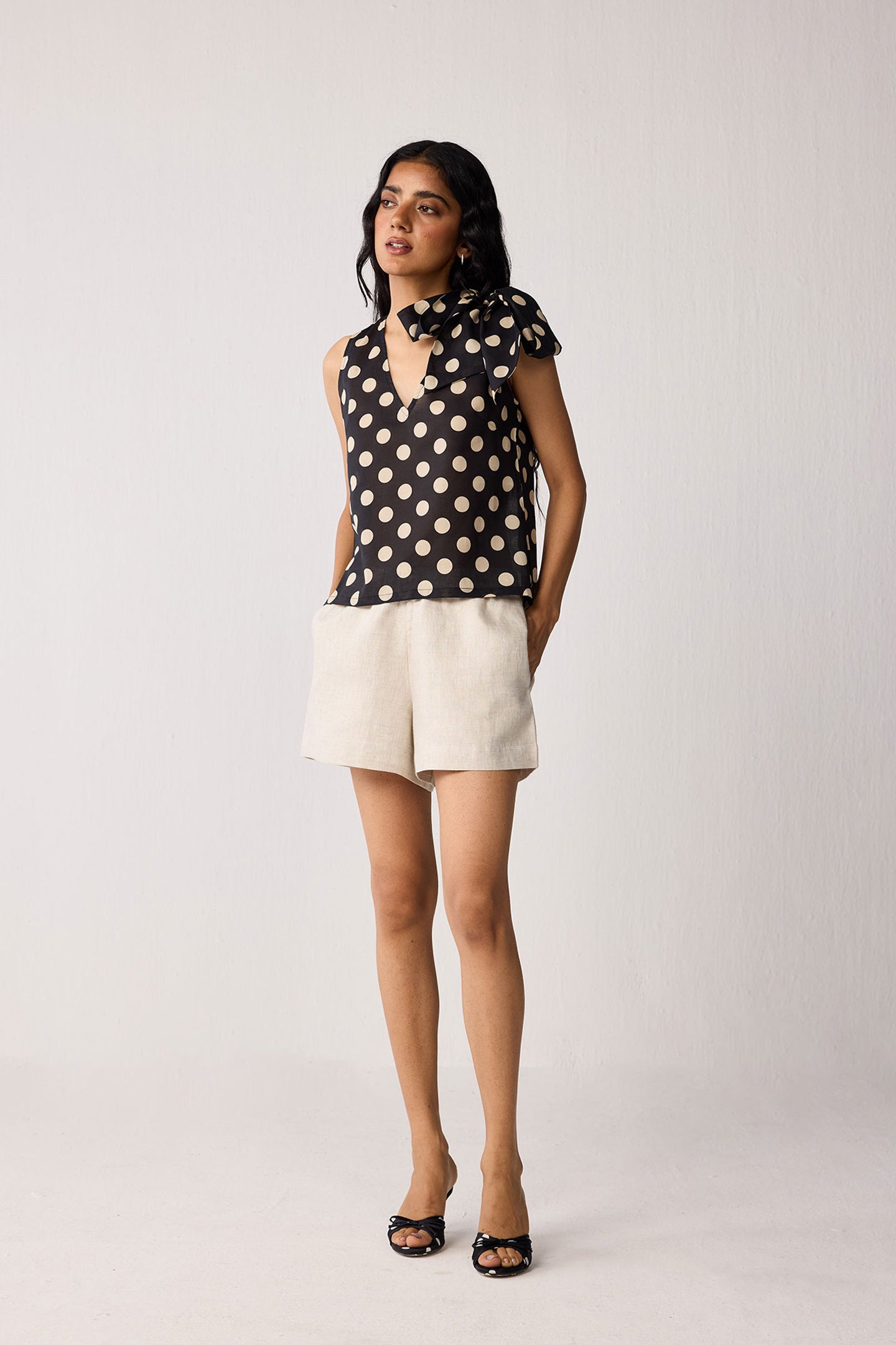 Woman wearing a black sleeveless top with beige polka dots and beige shorts on a white background
