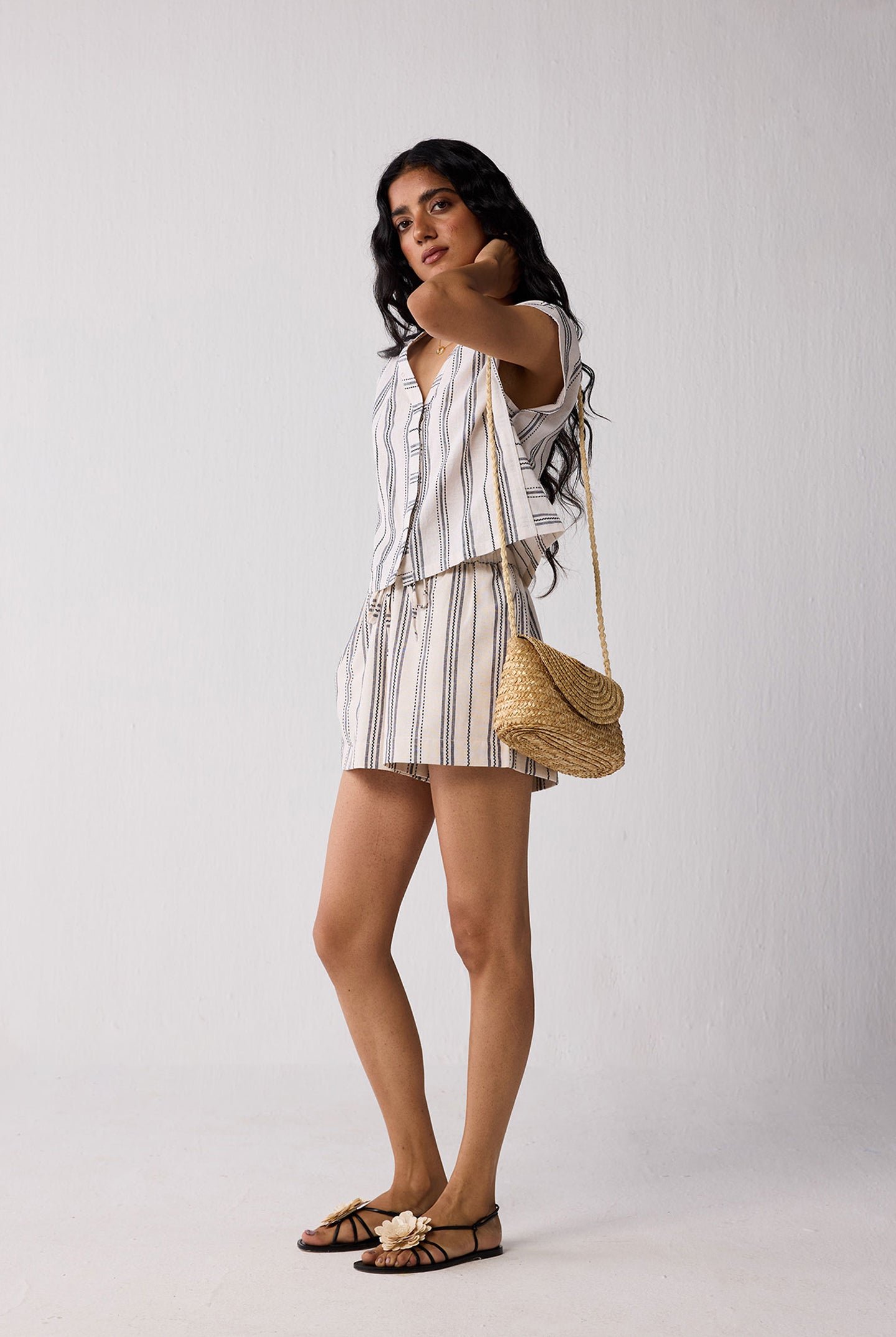 Woman in a striped outfit holding a straw bag against a white background