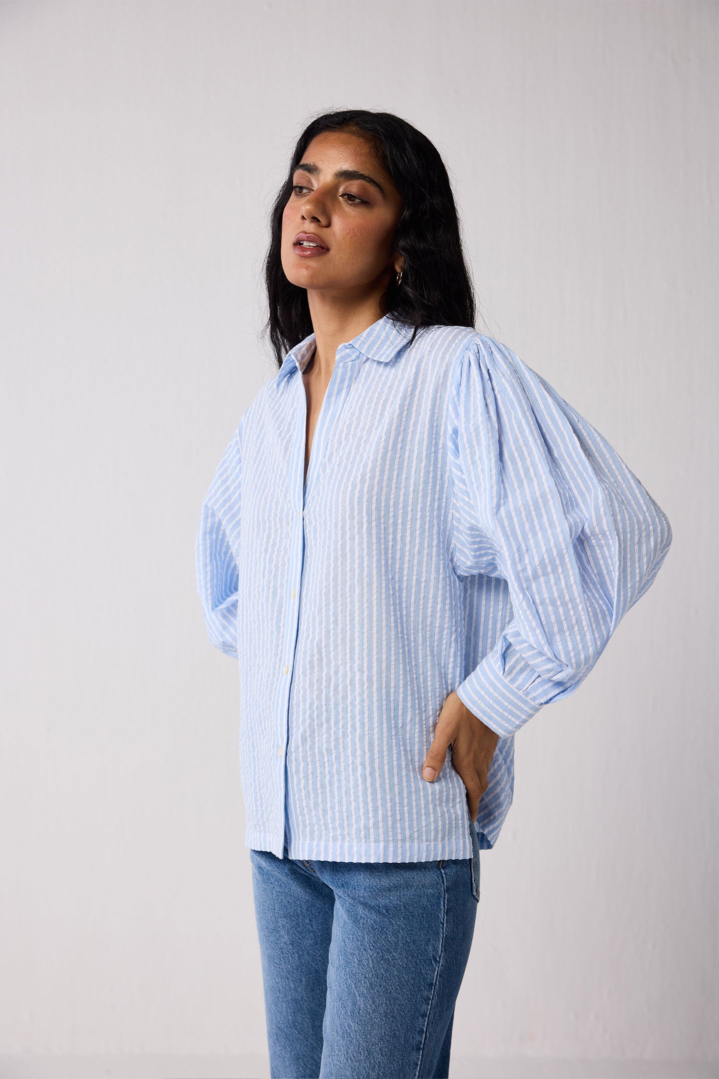 Woman wearing a light blue striped shirt and jeans against a plain background