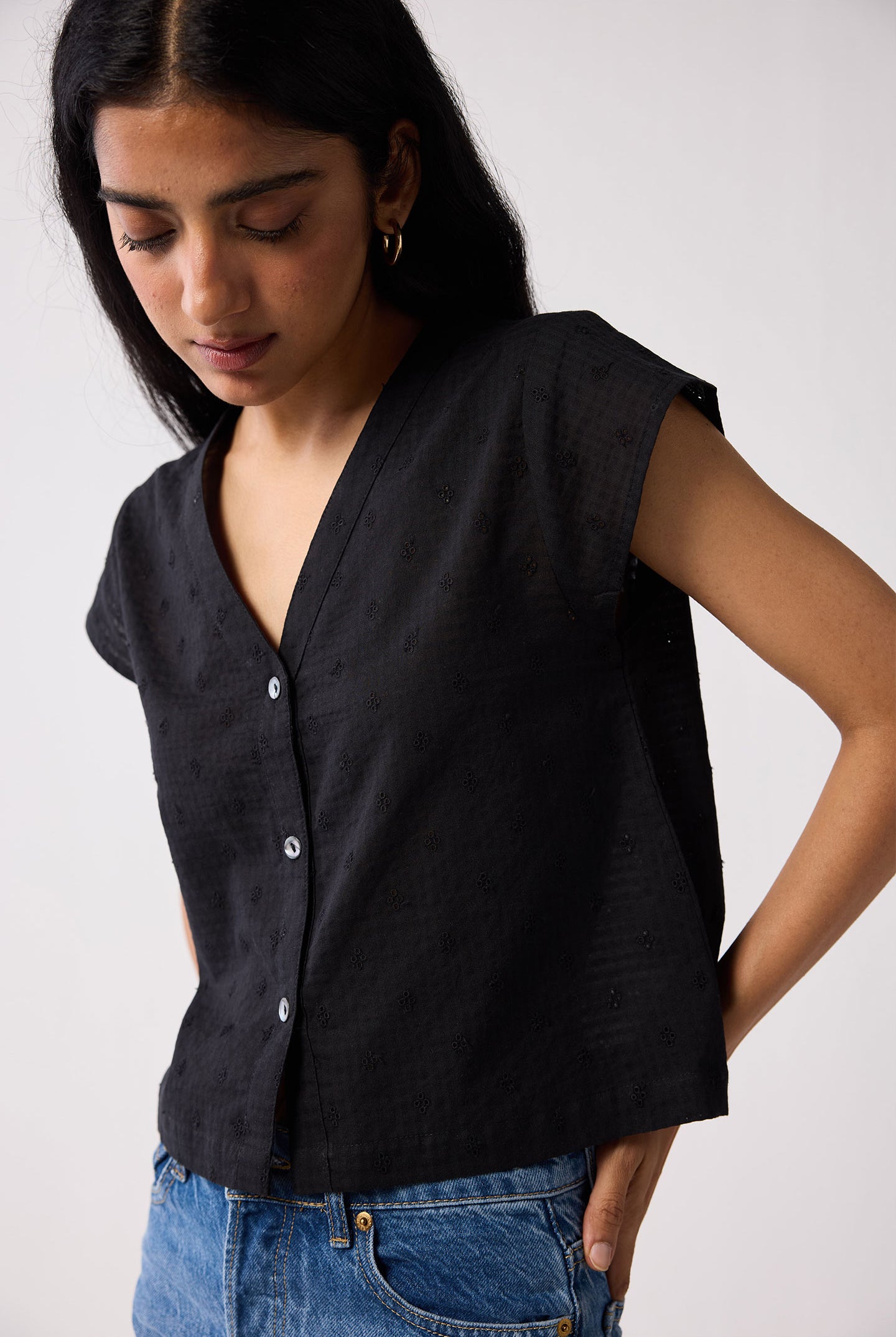 Woman wearing a black sleeveless shirt and blue jeans on a white background