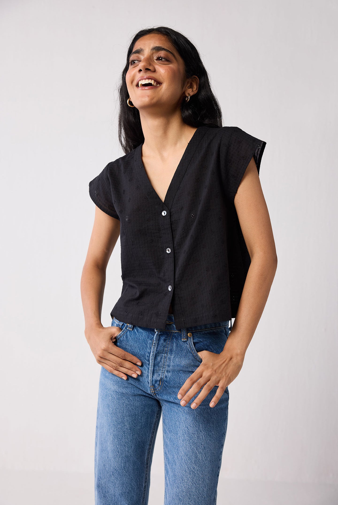 Woman wearing a black top and blue jeans against a plain background