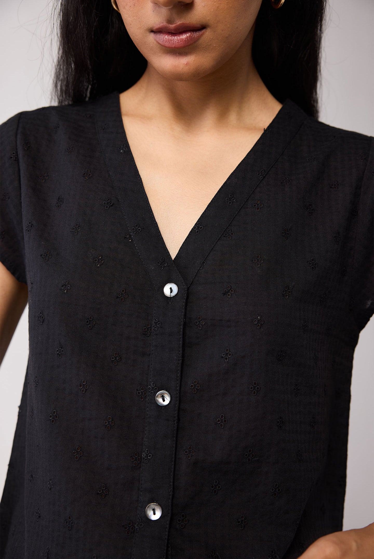 Black blouse with button details worn by a person on a plain background