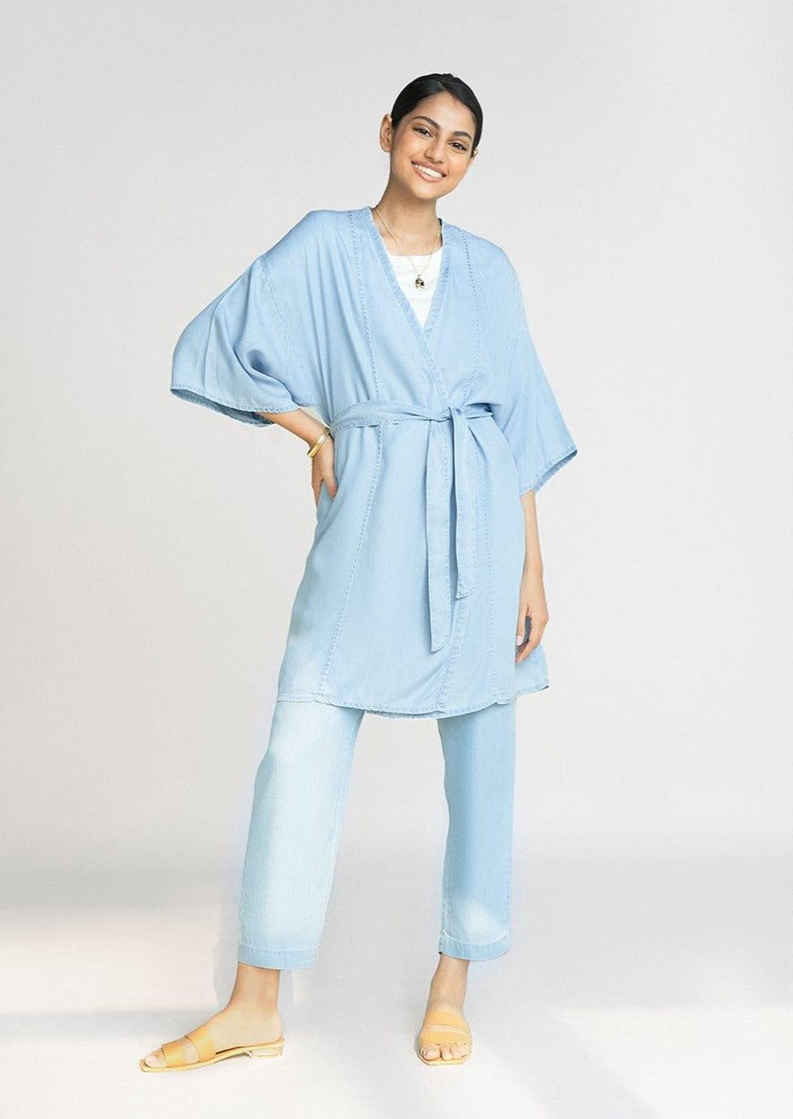 Model wearing the Reistor Wrapped in Happiness Overlay in Ocean Blue, showcasing a tie-waist design, airy fabric and a flowing contemporary silhouette.