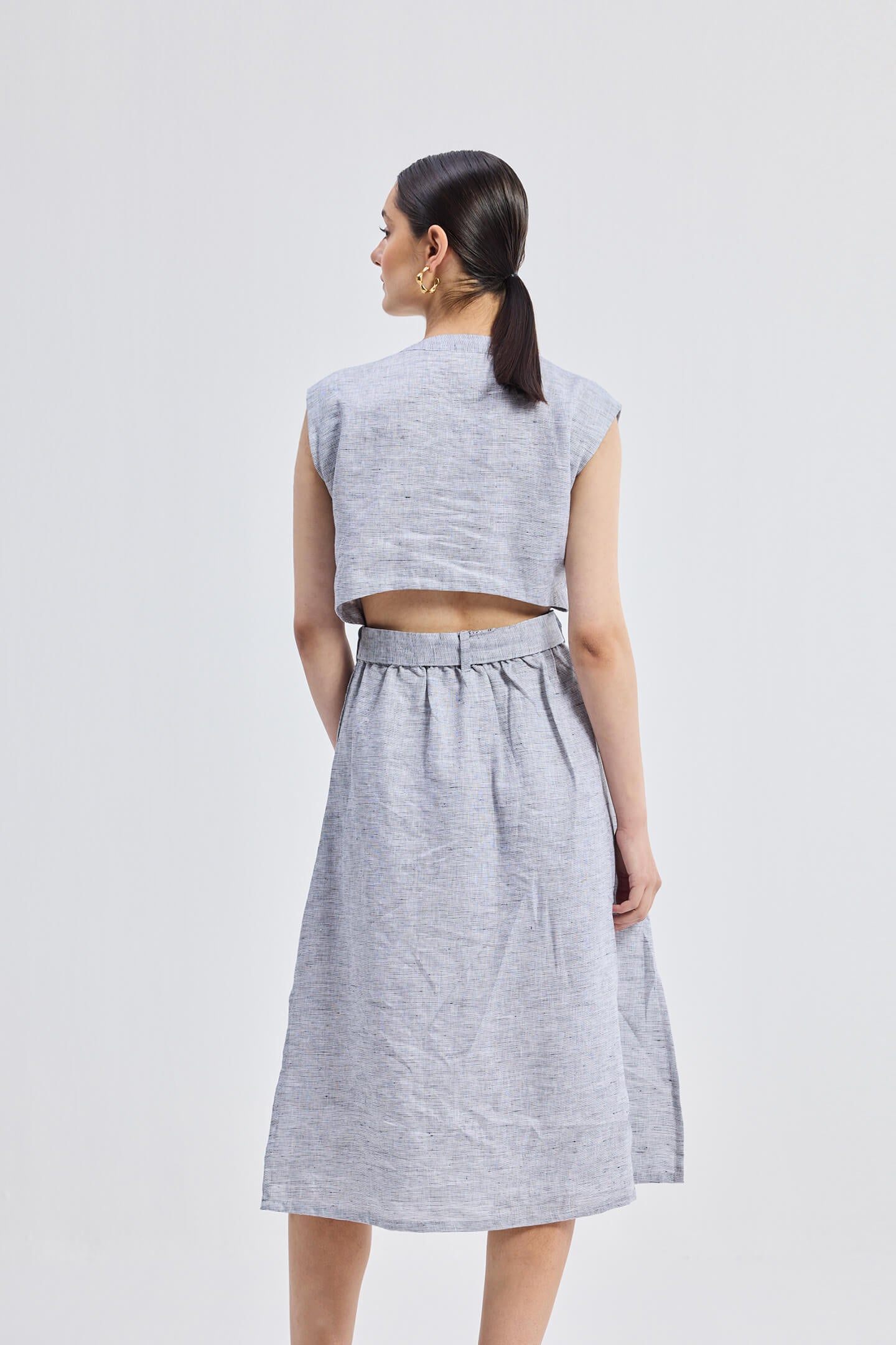 Back view of model wearing the Reistor Back Cut Out Linen Dress, showcasing the open back cut-out detail, sleeveless silhouette, and lightweight blue striped linen fabric.
