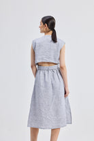 Back view of model wearing the Reistor Back Cut Out Linen Dress, showcasing the open back cut-out detail, sleeveless silhouette, and lightweight blue striped linen fabric.