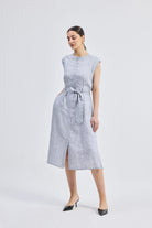 Full-length front view of model wearing the Reistor Back Cut Out Linen Dress, featuring a sleeveless design, button-down front, tie-waist belt, and light blue striped linen fabric.