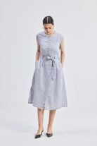 Model wearing reistor Back Cut Out Linen Dress in light grey, sleeveless midi-length linen dress with tie waist and front button detail.