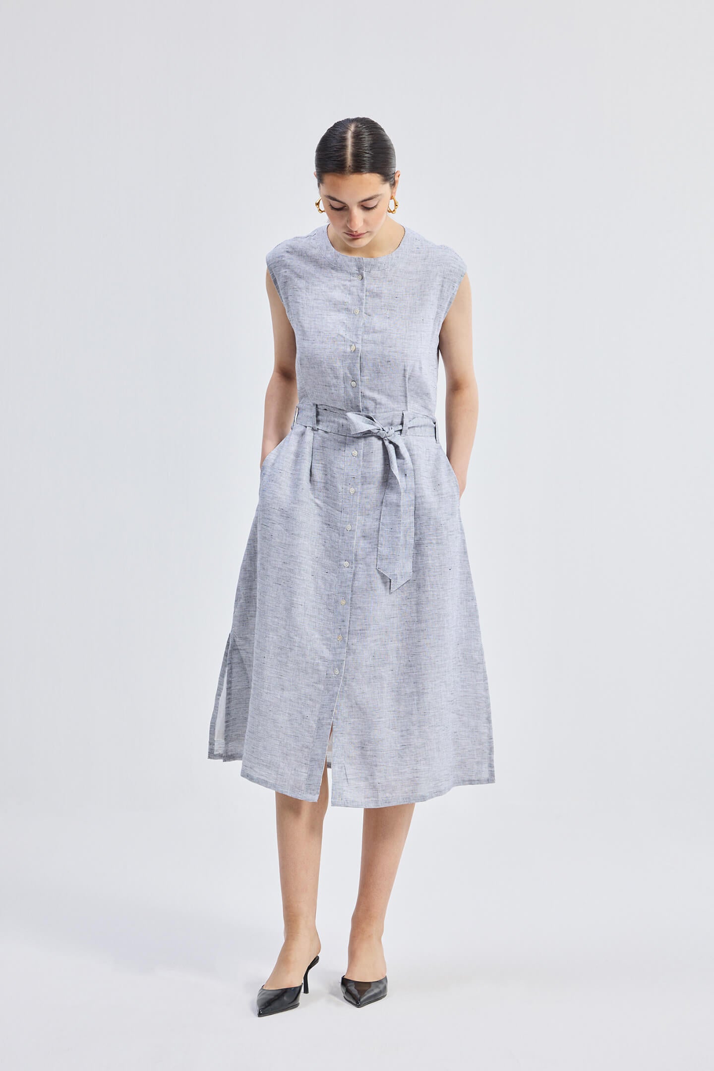 Model wearing reistor Back Cut Out Linen Dress in light grey, sleeveless midi-length linen dress with tie waist and front button detail.