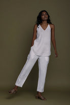 Woman wearing a Reistor white sleeveless top with Blankets on the Beach Pants against a brown background.