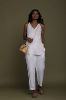 Reistor white sleeveless V-neck top with tapered pants, styled with a woven bag for sustainable women's fashion.