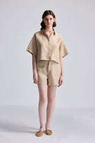 A model wearing a beige boxy shirt with lace detail on the shoulders and sleeves, paired with matching shorts.