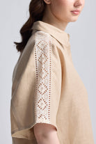 Front view of a woman wearing the beige Reistor Boxy Shirt with Lace, featuring a button-down front, collar, and relaxed fit.