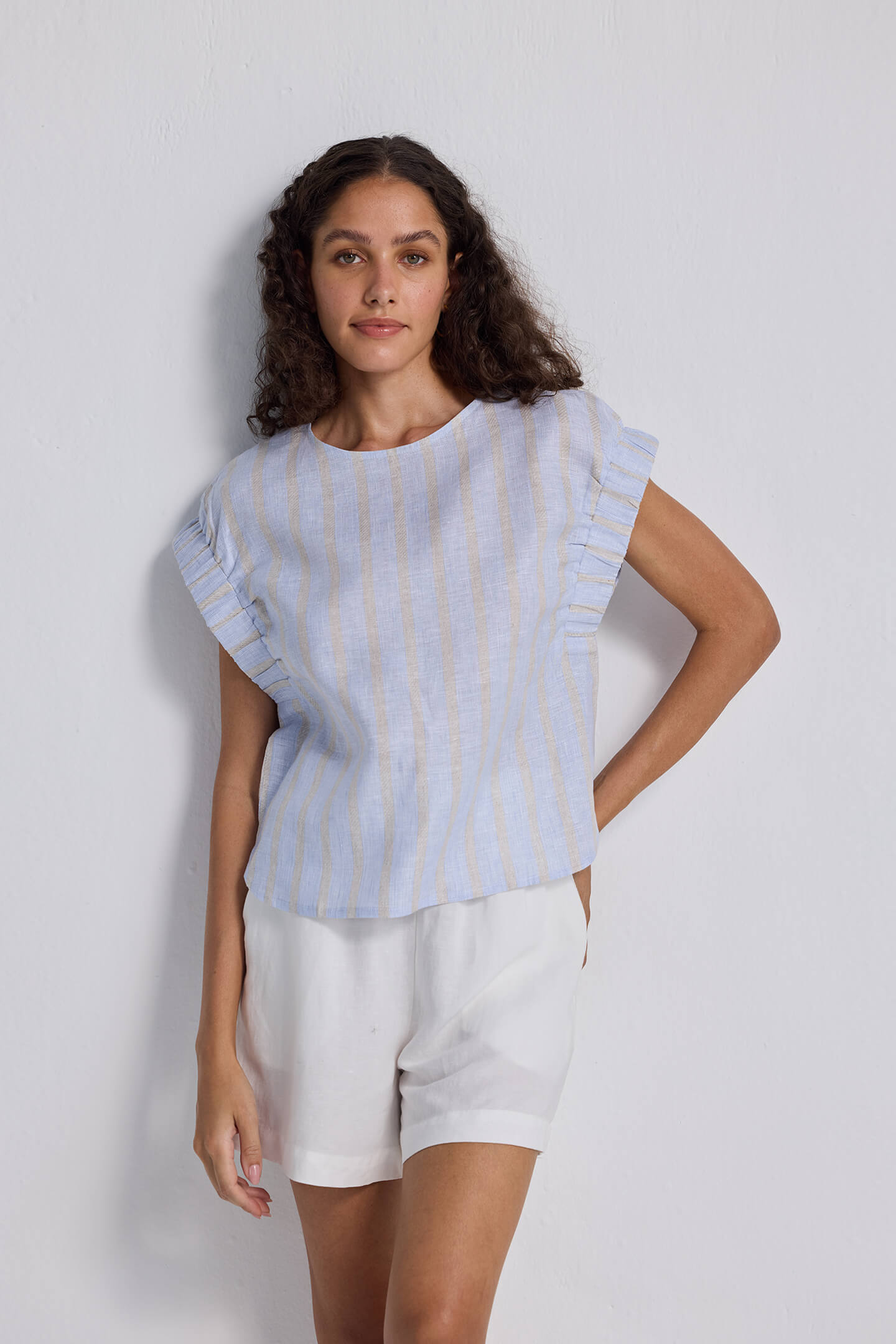 A woman wearing a boxy top with sleeve detailing and striped pattern. The top is light blue and white, and she is paired with white shorts.