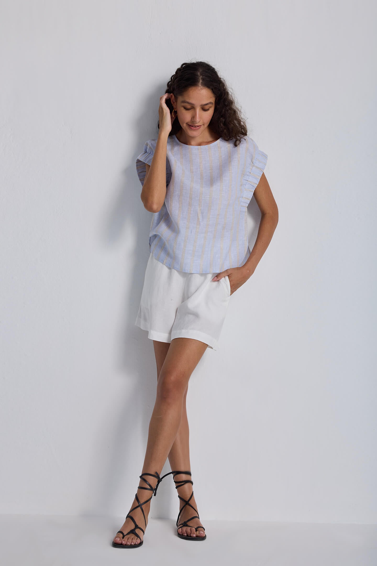 Model wearing a light blue striped Boxy Top with Sleeve Detailing by reistor, paired with white linen shorts and strappy black sandals.