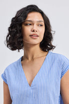 Model wearing the Reistor Boxy V-neck Top with Fray Detail, a blue and white striped sustainable women's top with frayed sleeve edges.