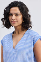Close-up of model wearing Reistor Boxy V-neck Top with Fray Detail in blue striped textured fabric, relaxed fit sustainable women’s top with frayed sleeve edges.