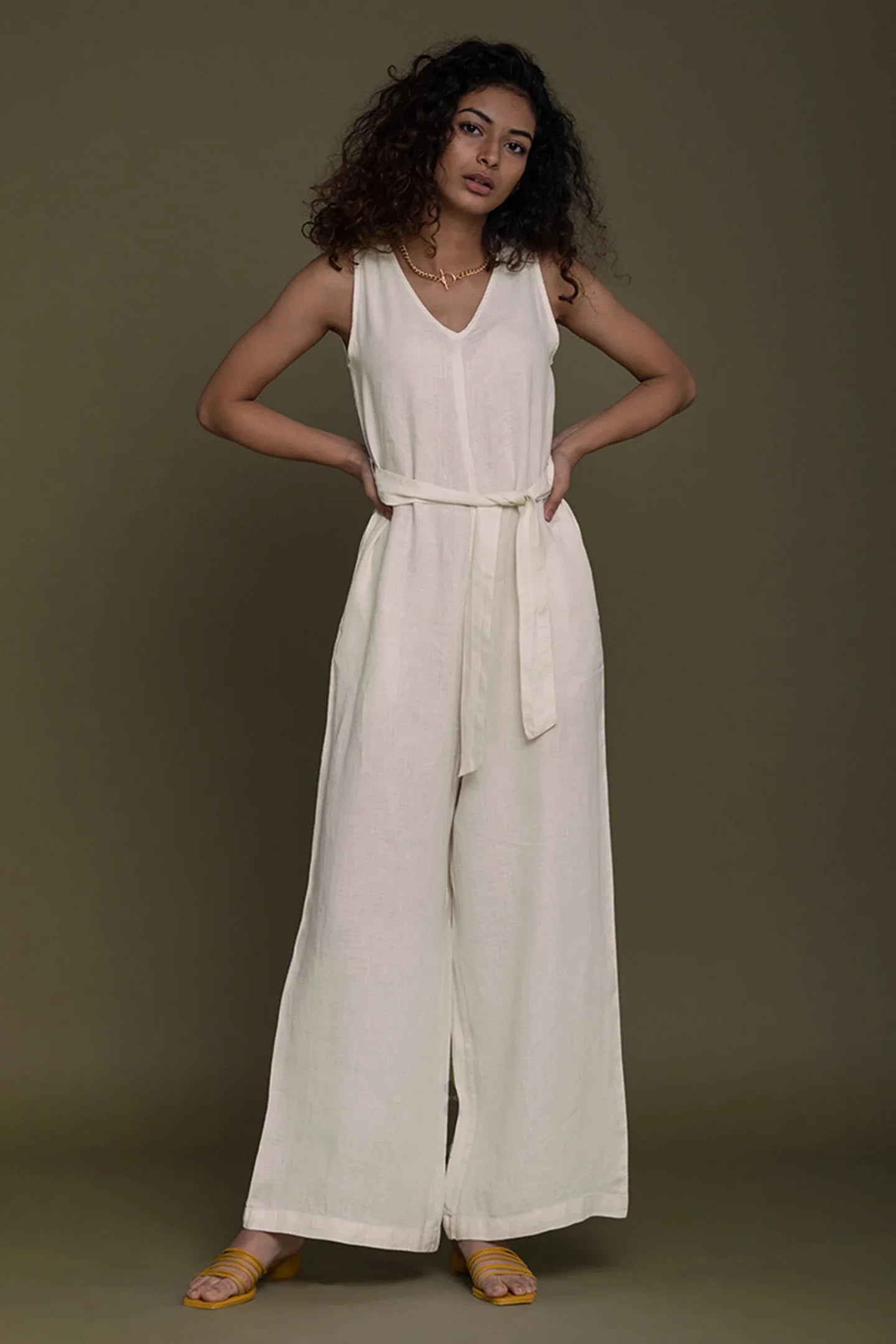 Model wearing a Reistor white sleeveless jumpsuit against a plain brown background.