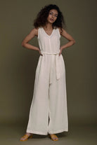 Model wearing a Reistor white sleeveless jumpsuit against a plain brown background.