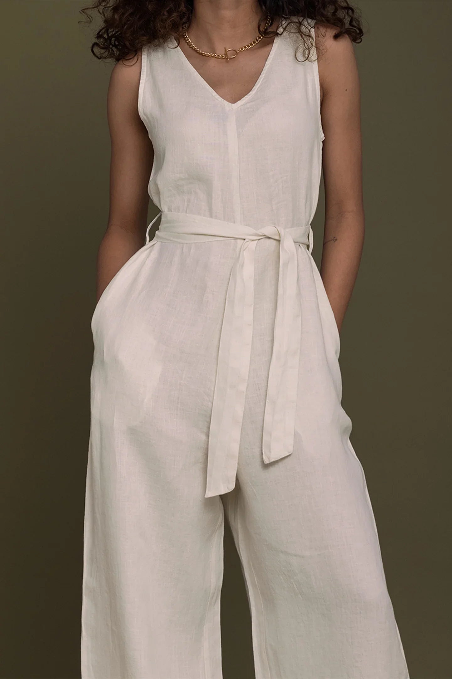 Person wearing a Reistor white sleeveless jumpsuit with a belt against a brown background.