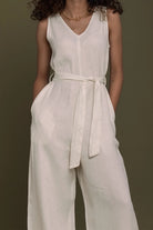 Person wearing a Reistor white sleeveless jumpsuit with a belt against a brown background.
