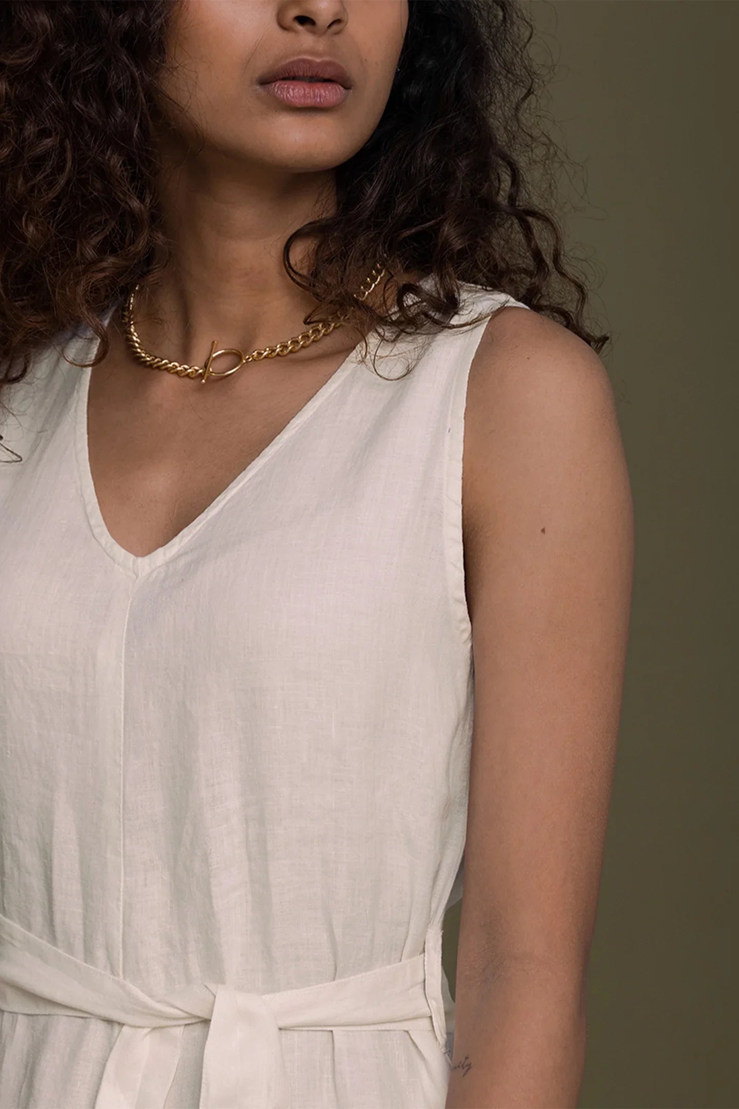 Close-up of Reistor sleeveless V-neck beige jumpsuit with tie waist, crafted for timeless sustainable women's fashion.