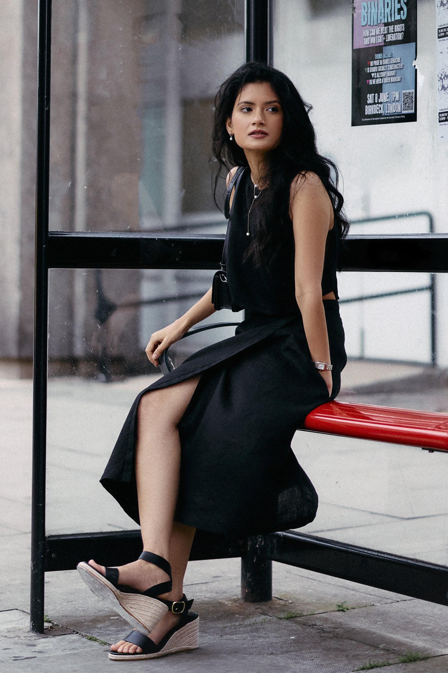 Model seated at a bus stop wearing Reistor Breezy Summer Set in Black, styled with a sleeveless crop top and flowy midi skirt, creating an effortless urban summer look.