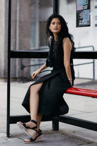 Model seated at a bus stop wearing Reistor Breezy Summer Set in Black, styled with a sleeveless crop top and flowy midi skirt, creating an effortless urban summer look.