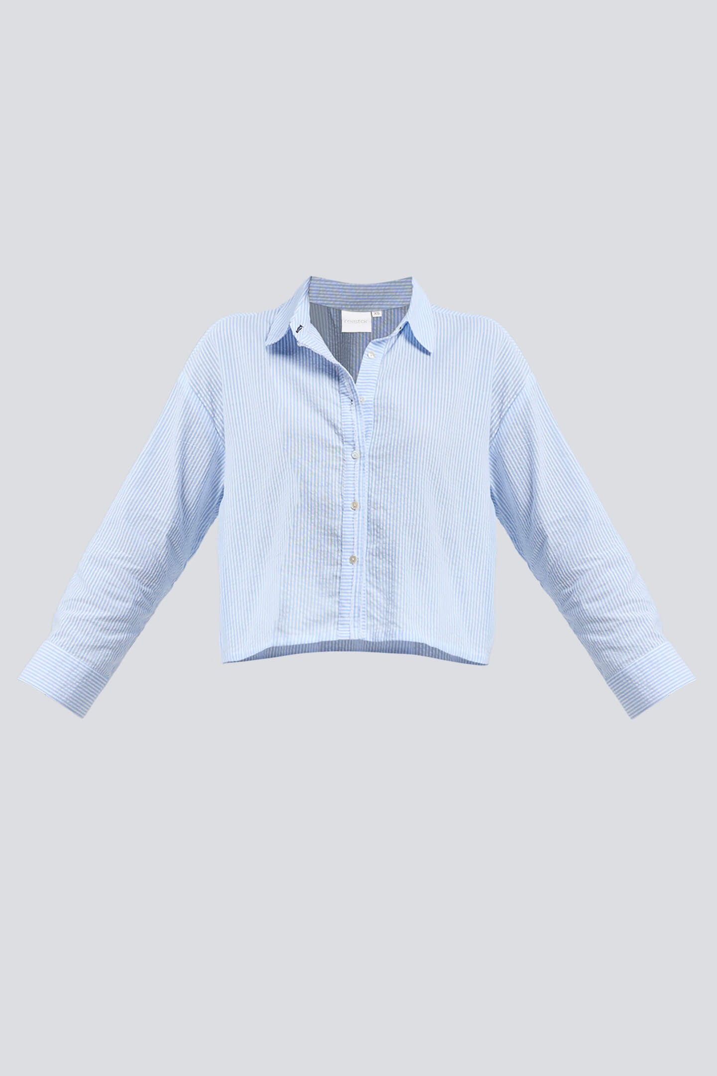 Front view of a model wearing the Reistor Crop it like it’s Hot Shirt in Stripes, featuring light blue and white vertical stripes, a relaxed cropped fit, and a classic button-down front paired with white trousers.