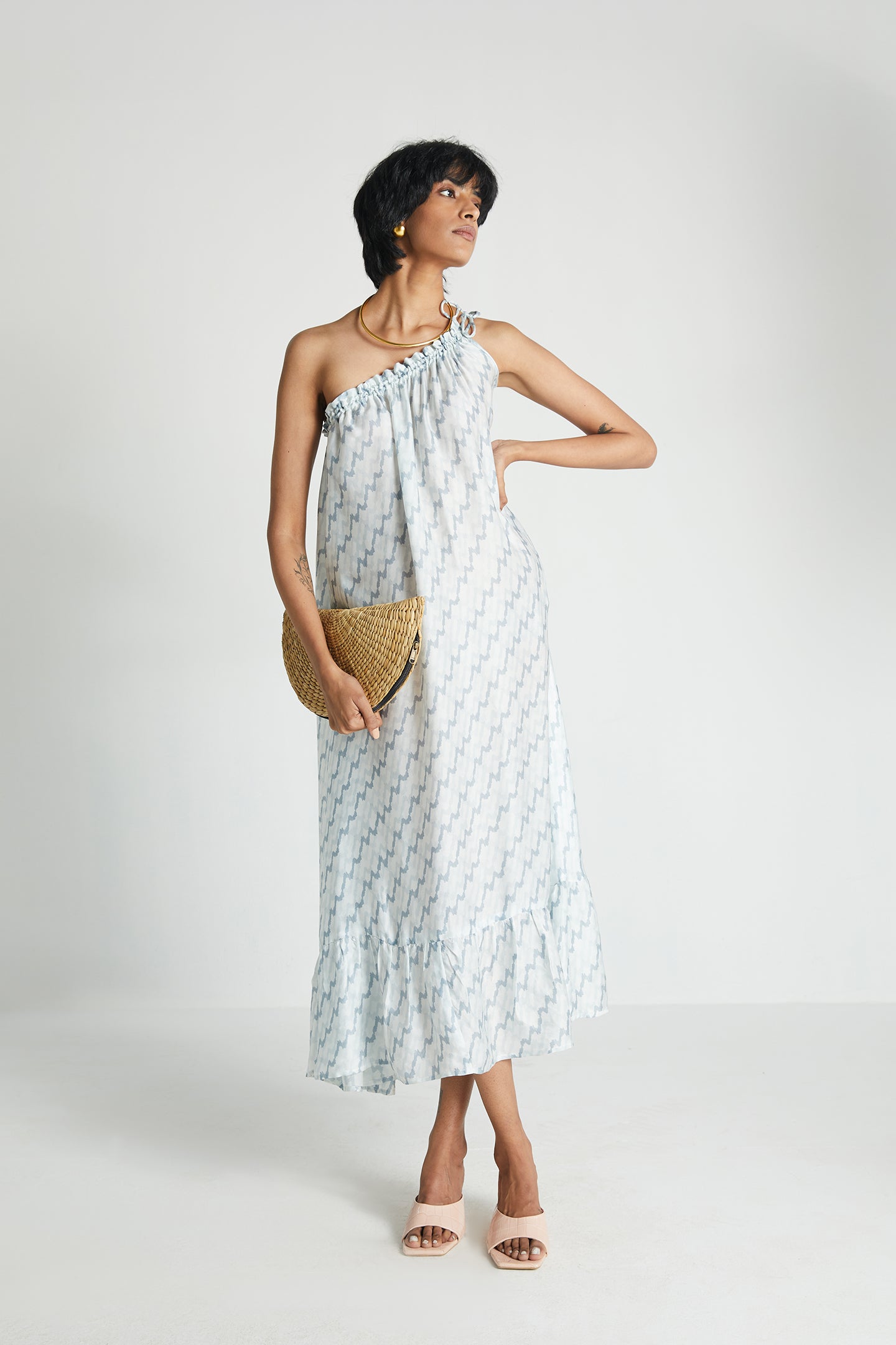 A model wearing a floral one-shoulder dress with a drawstring neckline, holding a clutch and wearing heels.