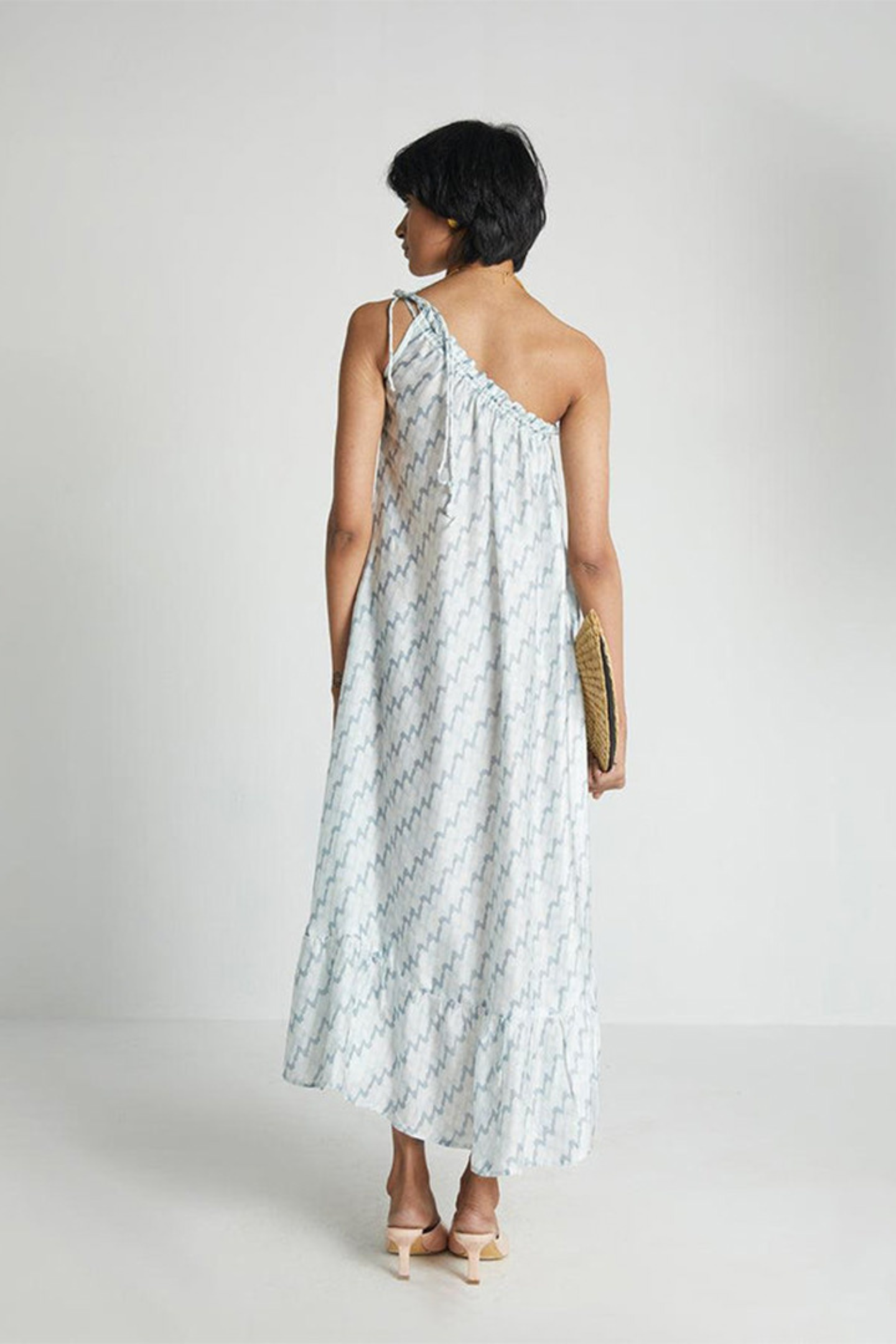 Woman wearing the Reistor Dancing in the Moonlight Dress, a light blue floral dress, holding a straw clutch against a white background for effortless summer style.