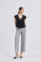 Deep V-neck short top in Black by reistor featuring cap sleeves, front button closure, and breathable linen fabric in a relaxed fit, styled with grey wide-leg pants, full-body view.