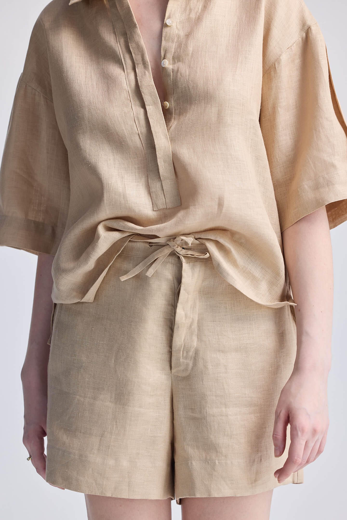 A close-up view of a model wearing reistor Drawstring Shorts in Neutral Beige, showing the adjustable tie waist and natural linen-look texture paired with a matching beige top.